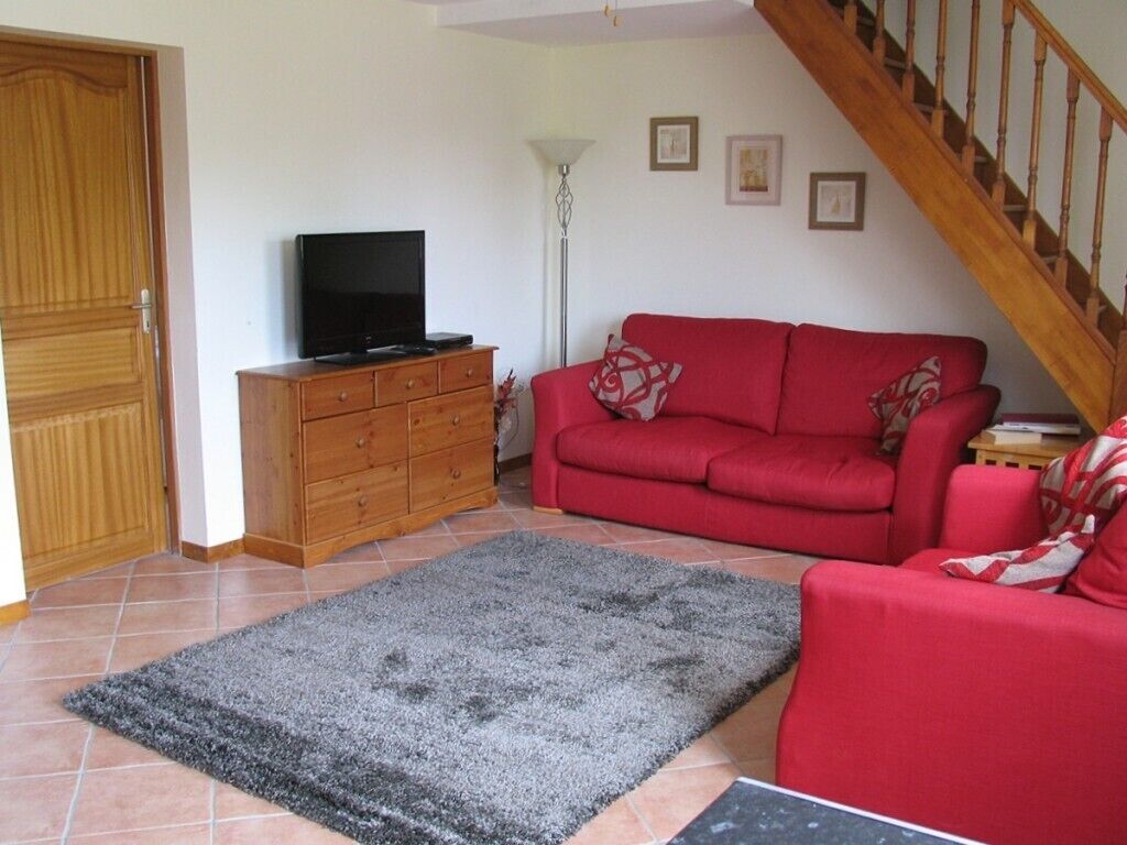 Ein Wohnzimmer mit einem roten Sofa, einem Fernseher auf einem Holzschrank, einem grauen Teppich und einer Treppe.