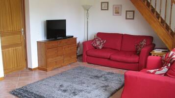 Ein Wohnzimmer mit einem roten Sofa, einem Fernseher auf einem Holzschrank, einem grauen Teppich und einer Treppe.