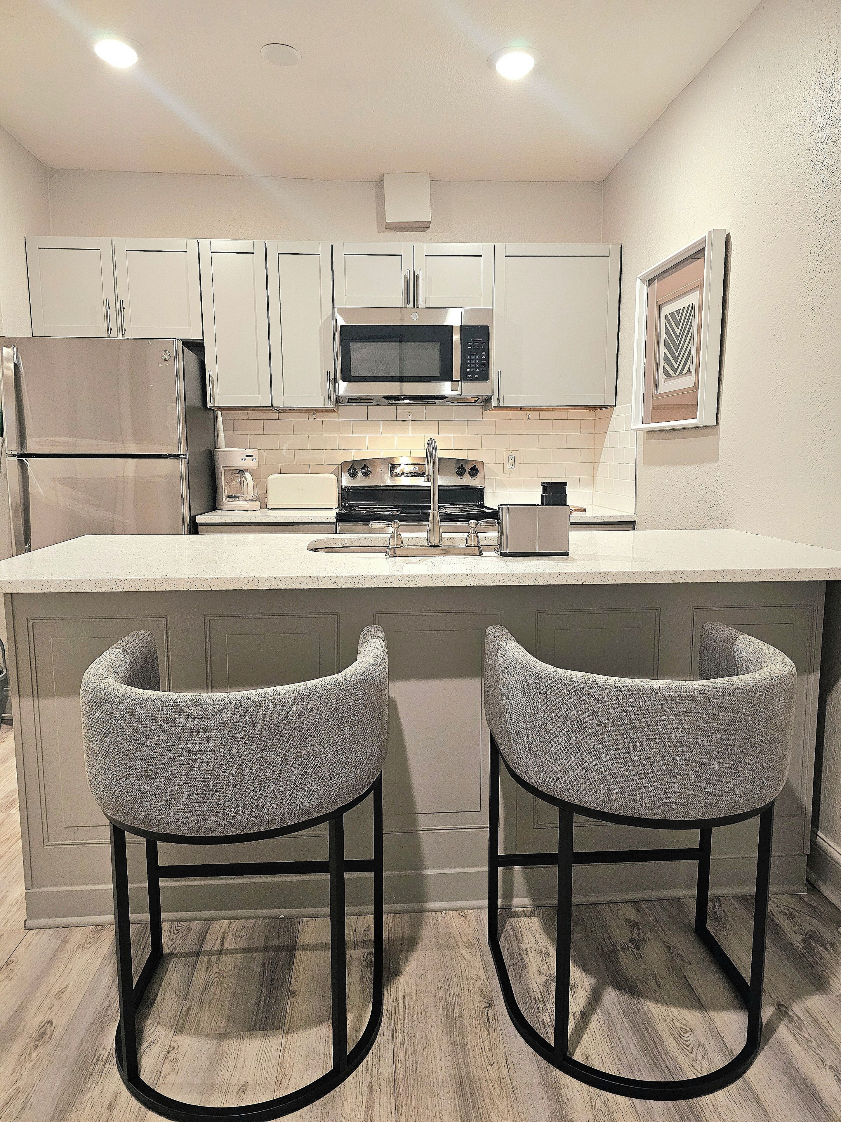 A modern kitchen with stainless steel appliances, a central island with bar stools, and a tiled backsplash.