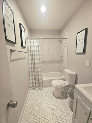 A bathroom with a shower, toilet, and sink. There are framed signs on the wall. - Cozy 1-bedroom apartment in charming KC's 'Squire Park with in-unit washer/dryer (Kansas City)