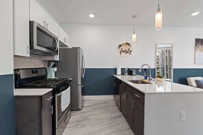 A modern kitchen with stainless steel appliances, a central island, and a 'family' sign on the wall. - Chic 1BR Stay | Sleeps 4 | Northern Liberties (Philadelphia)