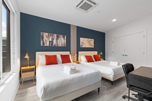A hotel room with two beds, a desk, and a chair. There are two wall-mounted artworks and a window with blinds. - Chic 1BR Stay | Sleeps 4 | Northern Liberties (Philadelphia)