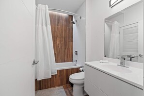 A modern bathroom with a wooden shower enclosure, a white toilet, and a large mirror above the sink. - Chic 1BR Stay | Sleeps 4 | Northern Liberties (Philadelphia)