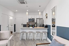 A modern kitchen with a central island, bar stools, and a dining area with a sofa. - Chic 1BR Stay | Sleeps 4 | Northern Liberties (Philadelphia)
