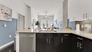 A modern kitchen with granite countertops, black cabinetry, and a built-in dishwasher. - Modern Uptown 1BR | Sleeps 4 | Near Klyde Park (Dallas)