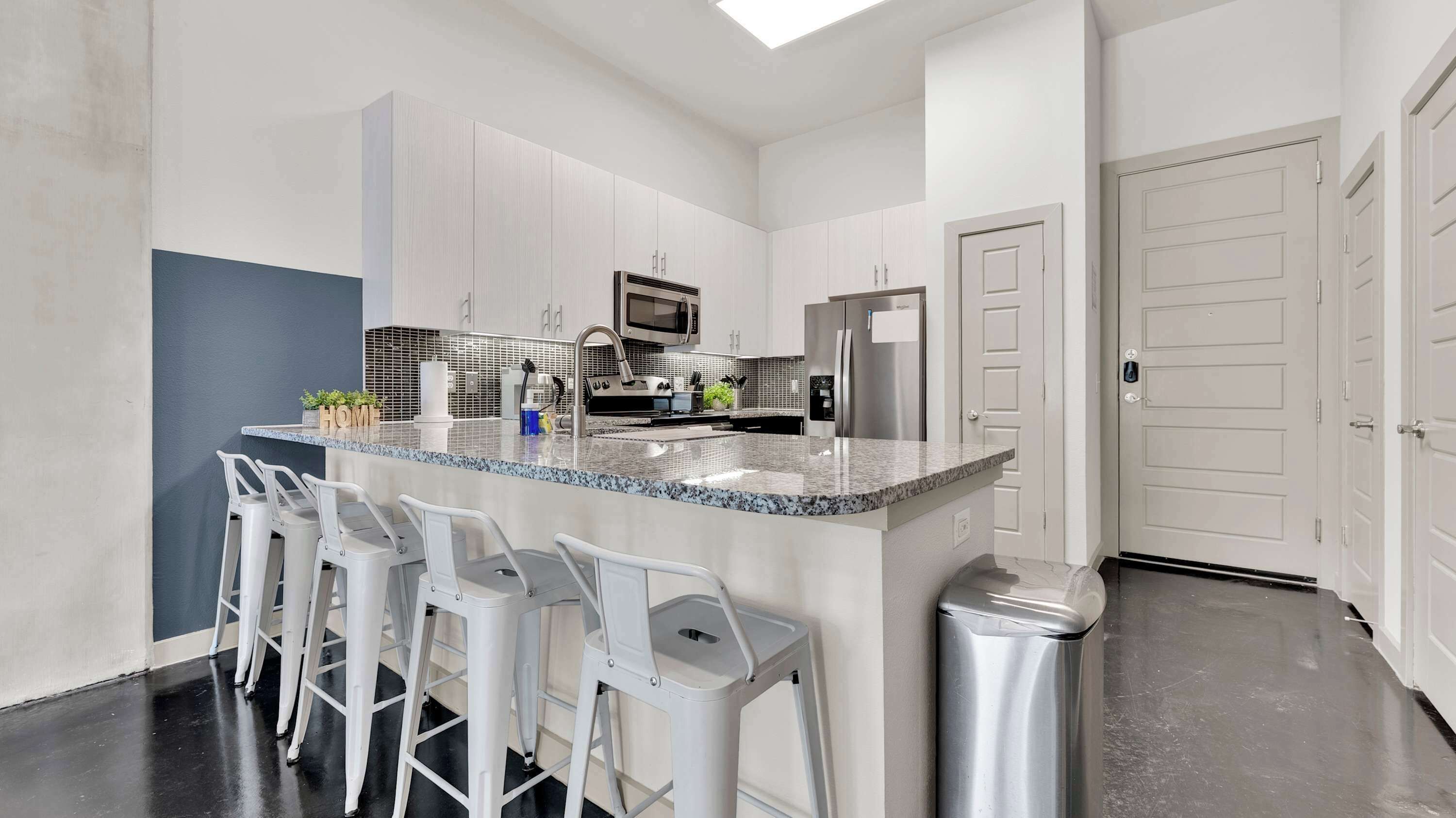 A modern kitchen with a central island, bar stools, stainless steel appliances, and a white door.