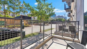 A balcony with a metal fence, a view of a parking lot, and buildings in the background. - Modern Uptown 1BR | Sleeps 4 | Near Klyde Park (Dallas)