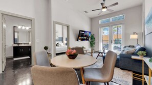 A modern living room with a round table, chairs, a sofa, a TV, and a ceiling fan. - Modern Uptown 1BR | Sleeps 4 | Near Klyde Park (Dallas)