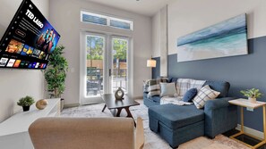 A modern living room with a sofa, a coffee table, and a TV mounted on the wall displaying a sports channel. - Modern Uptown 1BR | Sleeps 4 | Near Klyde Park (Dallas)