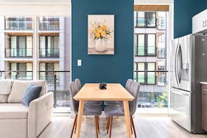 A modern apartment with a dining area, a kitchen, and large windows offering a view of a building with balconies. - Fresh 1BD Near City Hall | Comfortably Sleeps 2 (Philadelphia)