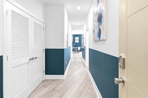 A hallway with a light wood floor, white and teal walls, and a door with a security lock. - Fresh 1BD Near City Hall | Comfortably Sleeps 2 (Philadelphia)