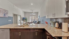 A modern kitchen with dark wood cabinets, granite countertops, and a built-in dishwasher. - Uptown 1BR | Sleeps 4 | Near Klyde Park (Dallas)