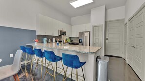 A modern kitchen with white cabinets, a stainless steel refrigerator, and a bar area with blue chairs. - Uptown 1BR | Sleeps 4 | Near Klyde Park (Dallas)