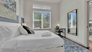 A hotel room with a bed, a desk, a chair, a mirror, and a window with blinds. - Uptown 1BR | Sleeps 4 | Near Klyde Park (Dallas)
