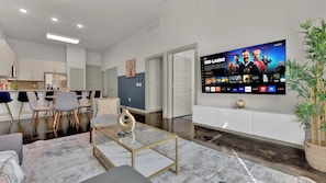 Uma sala de estar moderna com televisão de tela plana, uma mesa de centro de mármore e um espaço de refeições com cadeiras.
