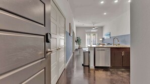 A hallway leading to a kitchen with a dishwasher, a ceiling fan, and a window with blinds. - Uptown 1BR | Sleeps 4 | Near Klyde Park (Dallas)