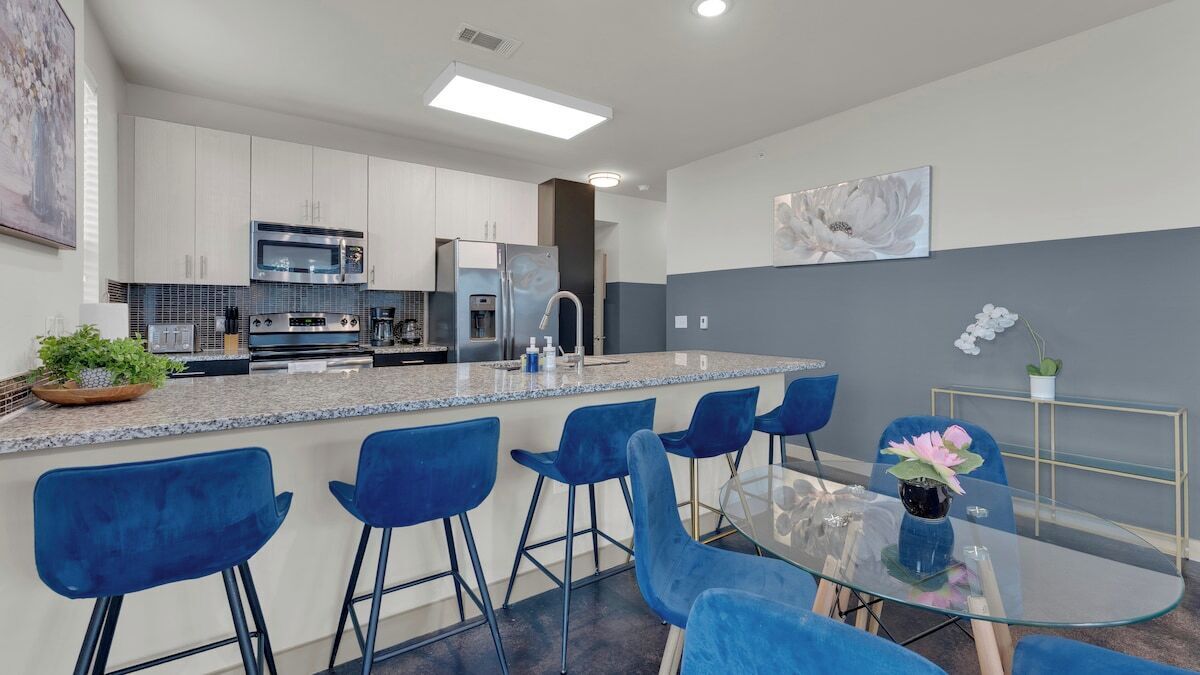 A modern kitchen with a central island, bar stools, and a glass dining table.
