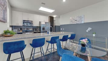 A modern kitchen with a central island, bar stools, and a glass dining table.