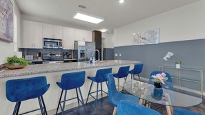 A modern kitchen with a central island, bar stools, and a glass dining table. - Uptown Escape 2BD | Sleeps 12 | Parking (Dallas)