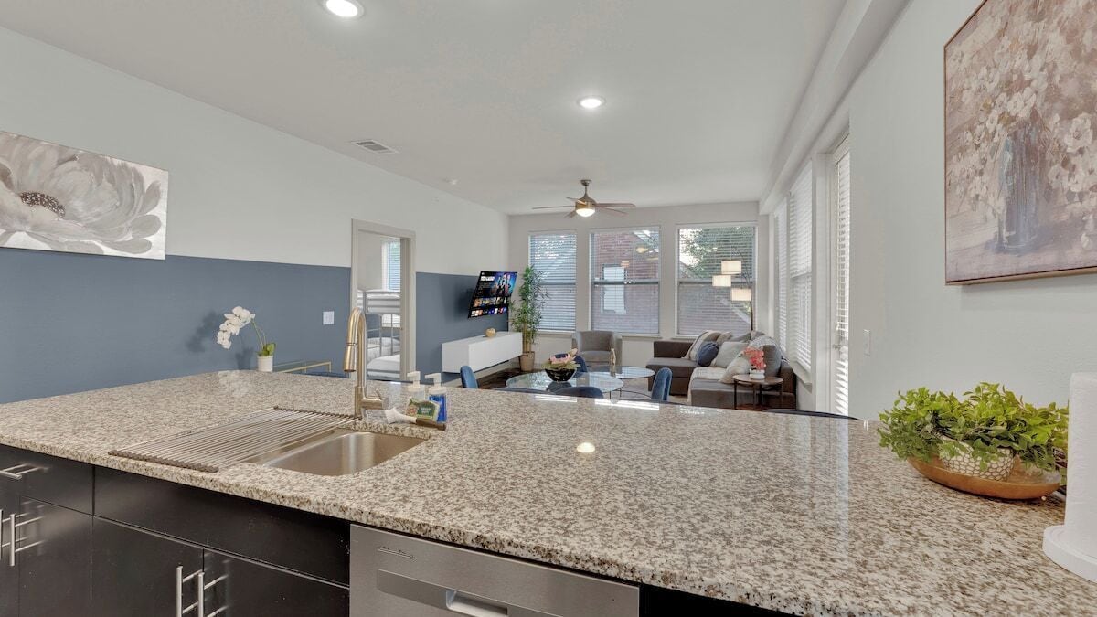 Una cocina moderna con encimeras de granito, lavavajillas integrado y un comedor con mesa y sillas.