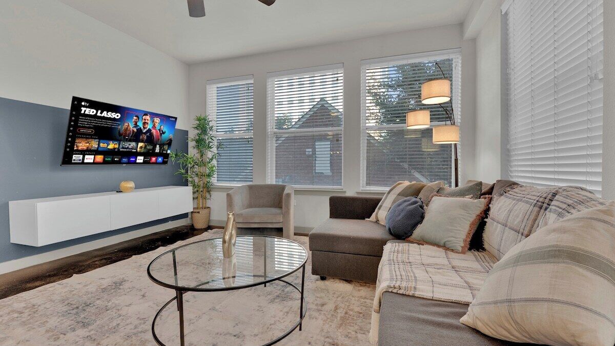 A living room with a flat-screen TV mounted on the wall, a glass coffee table, a sofa, and a chair.