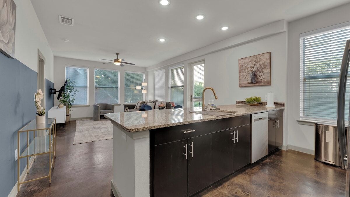 A modern kitchen with a central island, dark cabinetry, and a dining area with a sofa and chairs.