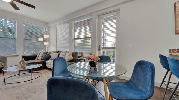 Un salon moderne avec une table basse en verre, des fauteuils à revêtement bleu, un canapé et un ventilateur de plafond.
