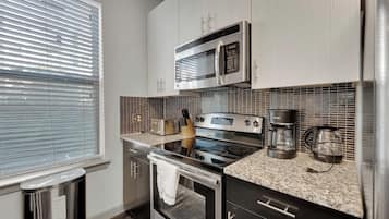 A modern kitchen with stainless steel appliances, a granite countertop, and a window with blinds.