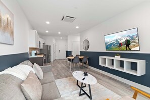 A modern living room with a sofa, dining table, and a TV mounted on the wall displaying a mountain scene. - Contemporary 1BR | Sleeps 2 | Northern Liberties (Philadelphia)