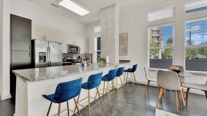 A modern kitchen with a central island, bar stools, and a dining area with a table and chairs. - Luxury 2BR Uptown | Sleeps 12 | Parking (Dallas)