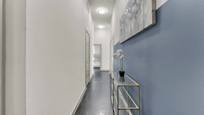A hallway with a glass table, a potted plant, and a bed visible in the distance. - Luxury 2BR Uptown | Sleeps 12 | Parking (Dallas)