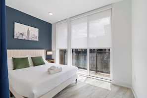 A modern bedroom with a large bed, a cityscape artwork, and a balcony with a view. - Spacious 3BR | Sleeps 8 | Northern Liberties (Philadelphia)