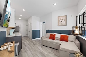 A modern living room with a sofa, a coffee table, and a TV mounted on the wall. - Spacious 3BR | Sleeps 8 | Northern Liberties (Philadelphia)