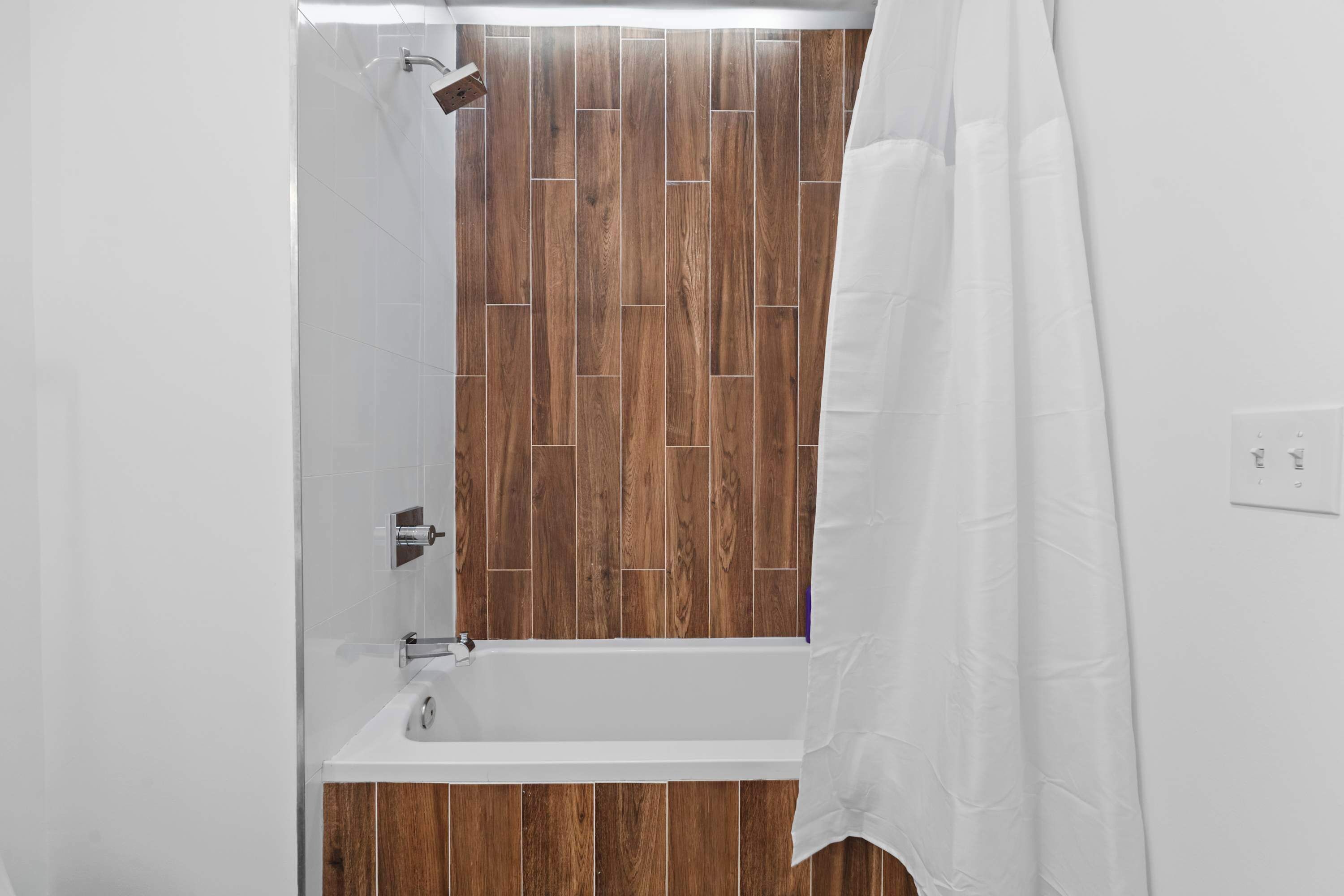 A bathroom with a wooden panel wall, a white bathtub, and a shower curtain.