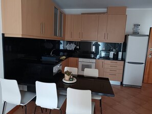 A modern kitchen with wooden cabinets, a black countertop, and a white dining table with chairs.