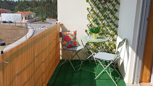 A balcony with a green artificial turf floor, a folding table, a chair, and a potted plant.