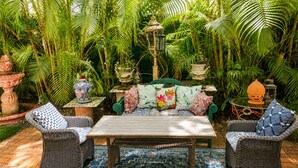 Eine tropische Garten-Terrasse mit Korbmöbeln, einem gemusterten Teppich und dekorativen Pflanzgefäßen.