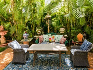 Eine tropische Garten-Terrasse mit Korbmöbeln, einem gemusterten Teppich und dekorativen Pflanzgefäßen.