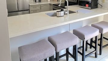 Une cuisine moderne dotée d’un îlot central, d’appareils électroménagers en acier inoxydable et d’un dosseret carrelé.