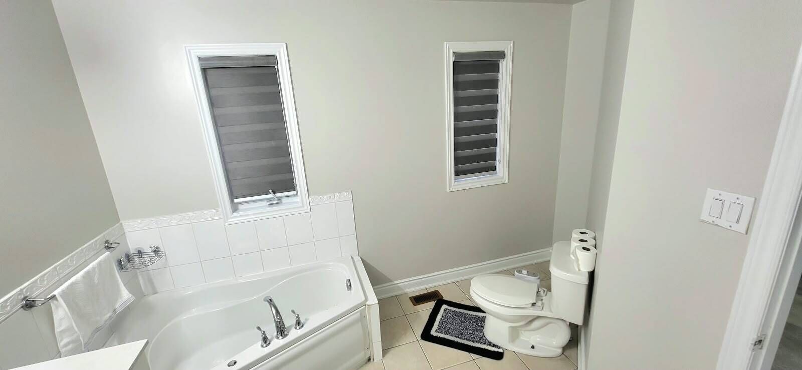 Une salle de bain avec une baignoire, des toilettes et deux fenêtres.
