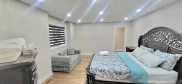 Ein Schlafzimmer mit einem Bett, Nachttischen, einem Sofa, einem Fenster mit Jalousien und einer Tür.