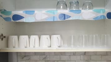 Une cuisine avec un plan de travail blanc, un grille-pain et des étagères où sont rangées des tasses et des verres.
