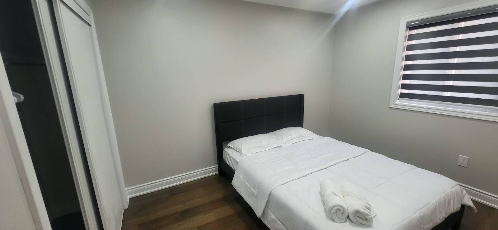 Une petite chambre à coucher, bien aménagée, avec un lit simple, une tête de lit sombre et une fenêtre avec des stores.