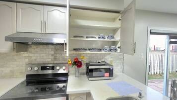 Una cocina con gabinetes blancos, una campana de acero inoxidable, un microondas y un lavamanos.