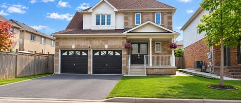 A two-story residential house with a front porch, two garage doors, and a well-maintained lawn.