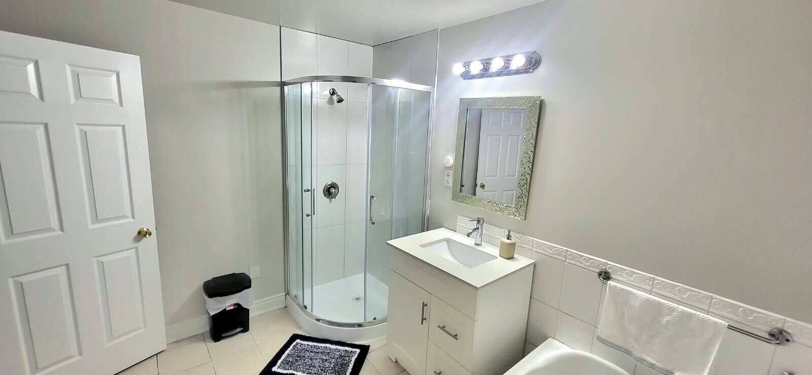 A bathroom with a glass-enclosed shower, a white sink, a mirror with a decorative frame, and a white toilet.