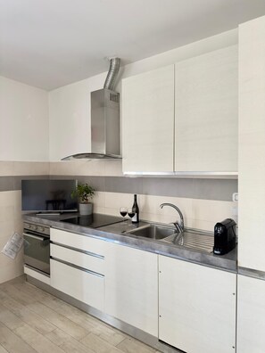 A modern kitchen with a stainless steel range hood, a double sink, and a coffee maker.