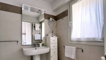 Un bagno moderno con un lavabo su piedistallo, uno specchio, un porta asciugamani e una finestra con tende.