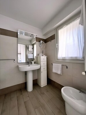 A modern bathroom with a pedestal sink, a mirror, a towel rack, and a window with curtains.