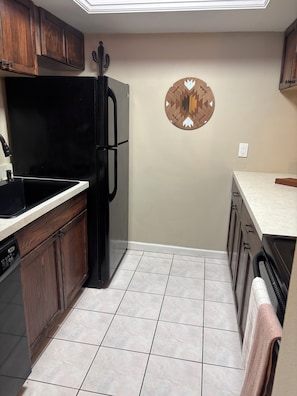 A compact kitchen with a black refrigerator, wooden cabinets, a sink, and a decorative wall piece.